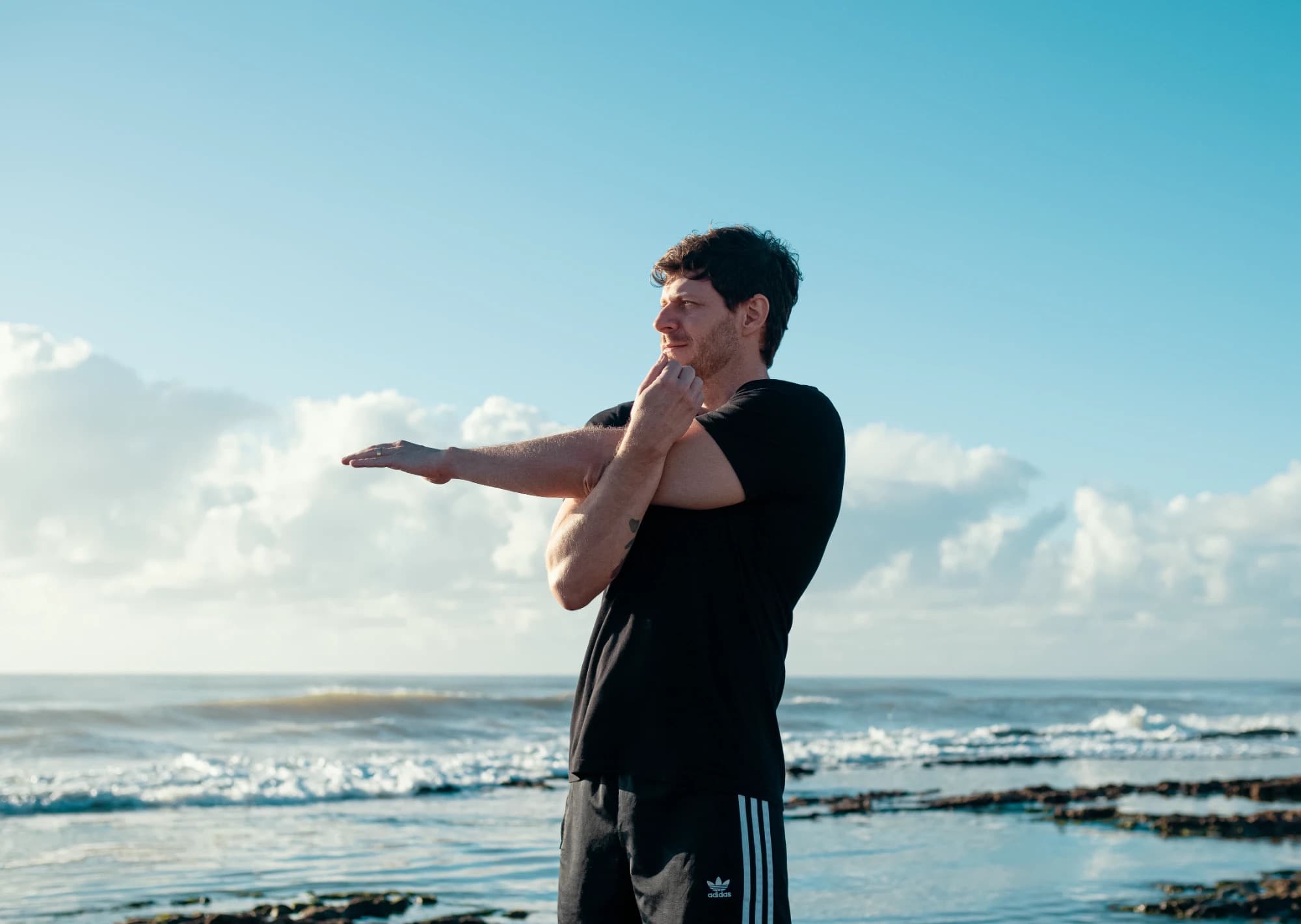 Homem alongando o braço em frente ao mar